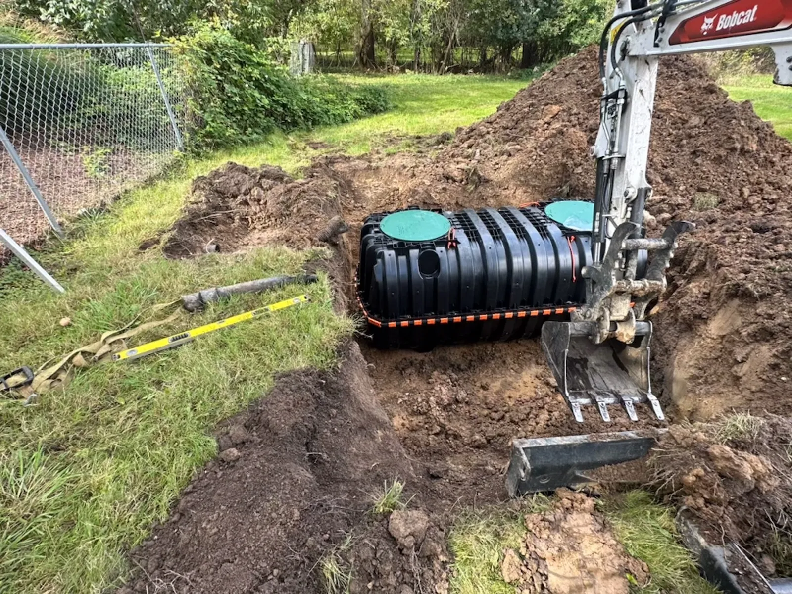 Excavator positioning a septic tank over the excavation